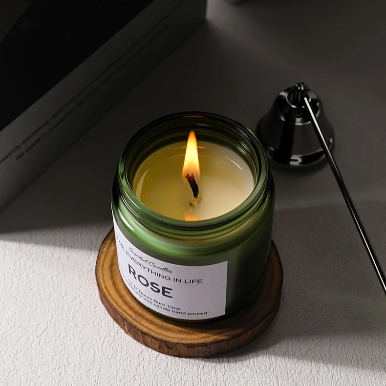 Candle in a green jar with a wooden coaster on a light surface.