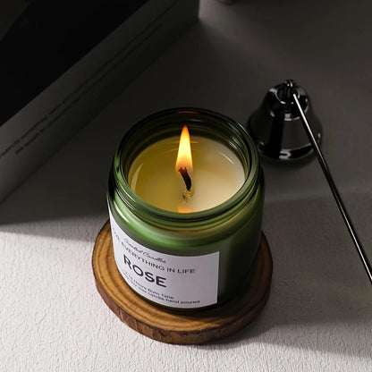 Candle in a green jar with a wooden coaster on a light surface.