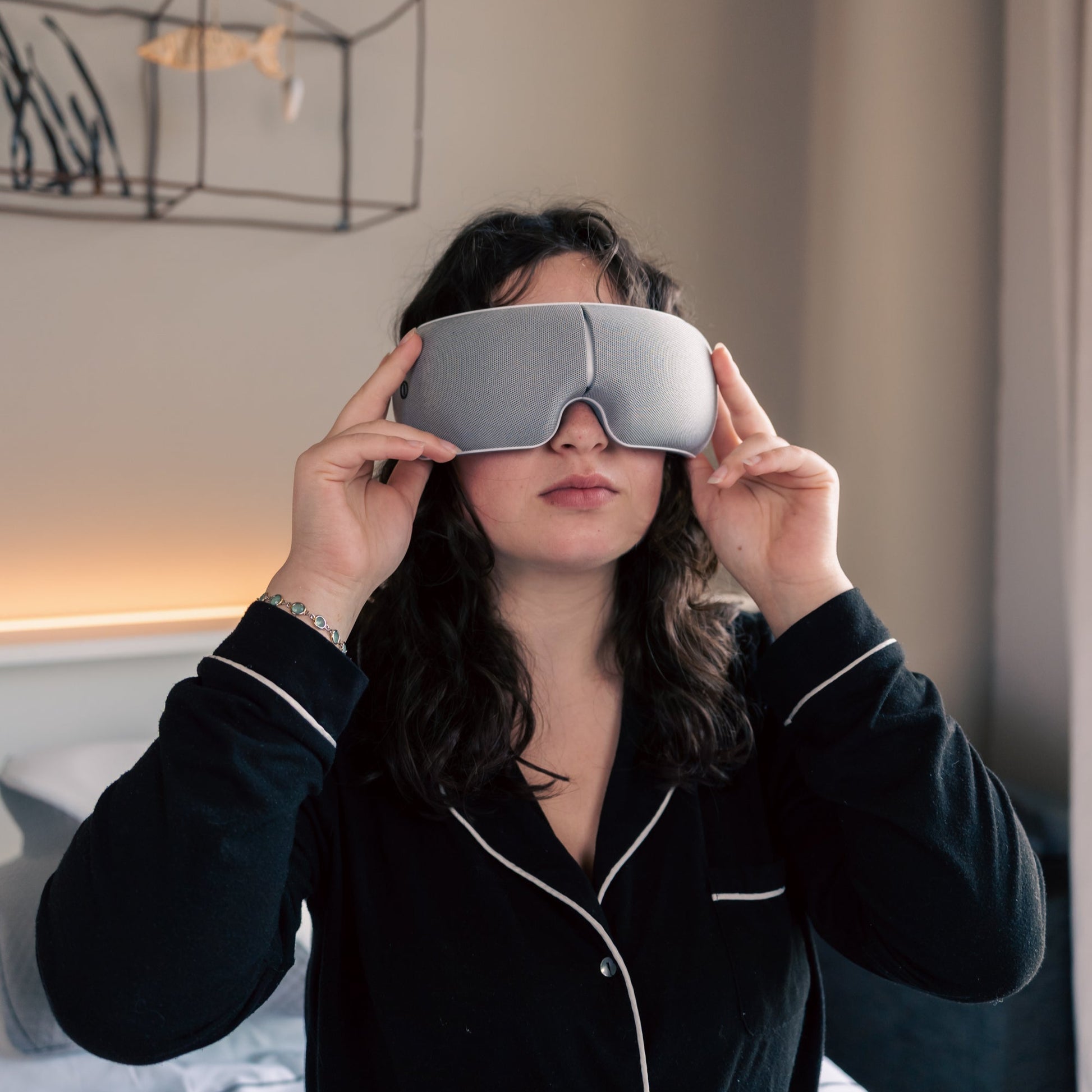 Person wearing a black outfit holding a silver sleep mask in front of their face.