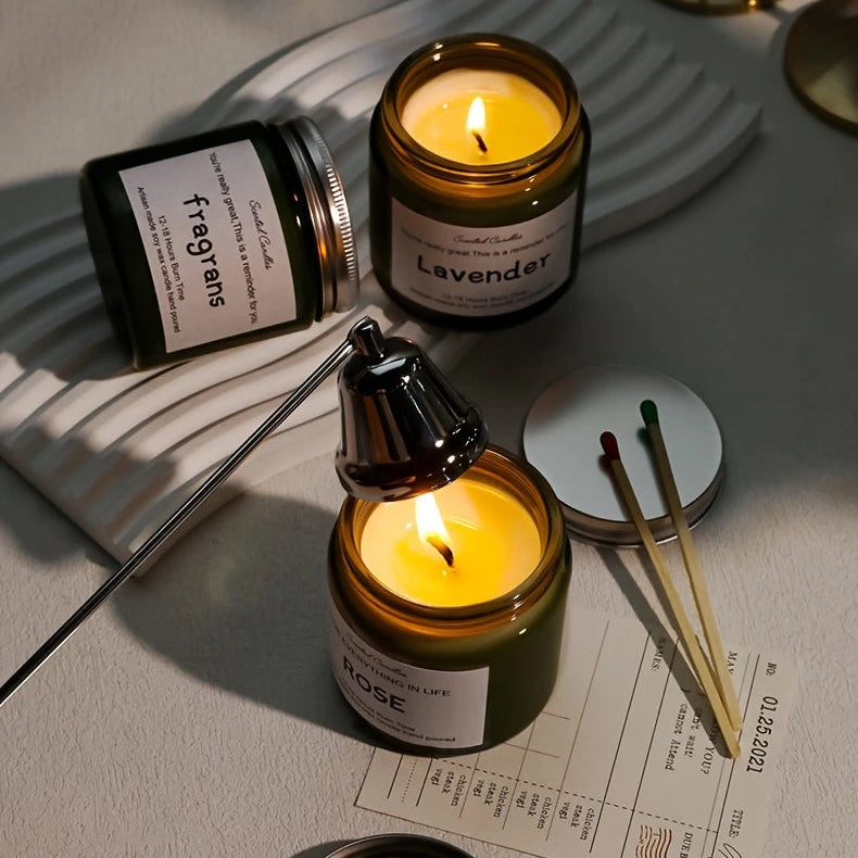 Two lit candles in glass jars with labels on a light surface.